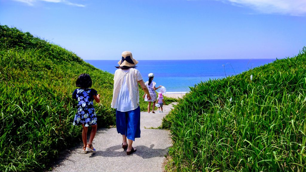 丘の向こうに見える海と海へ向かって歩く家族
