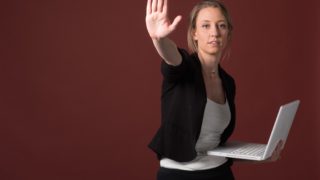 パソコン片手に手を上げている外国人女性